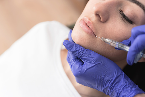 Closeup cropped image of doctor's hands injecting filler in lower lip of patient , Aesthetic corrective treatments concept